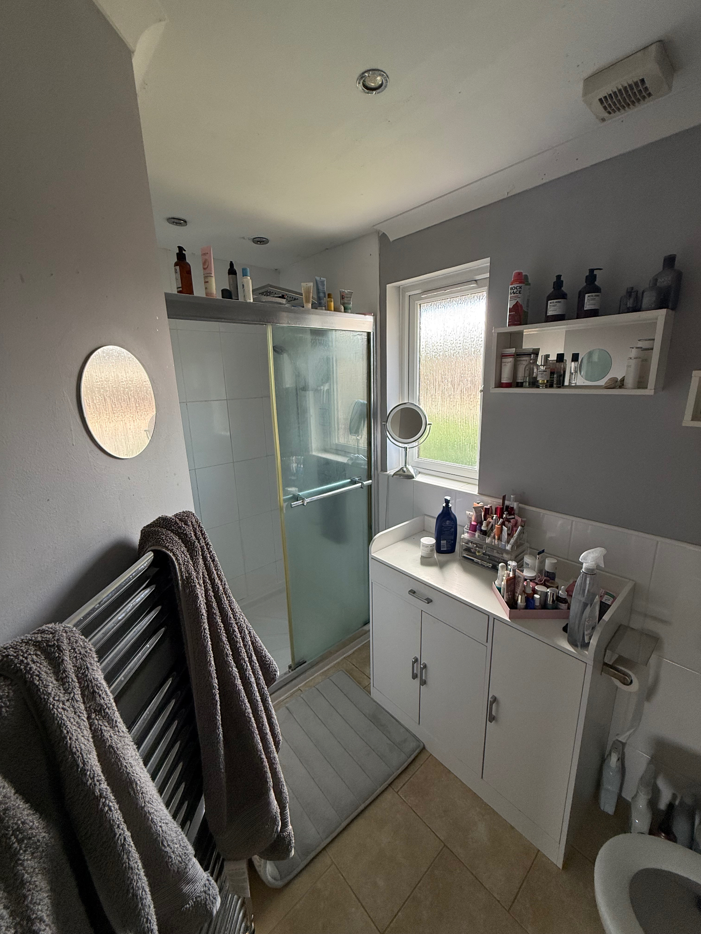 Before — dated bathroom with sliding shower door, cluttered shelves and old tiling